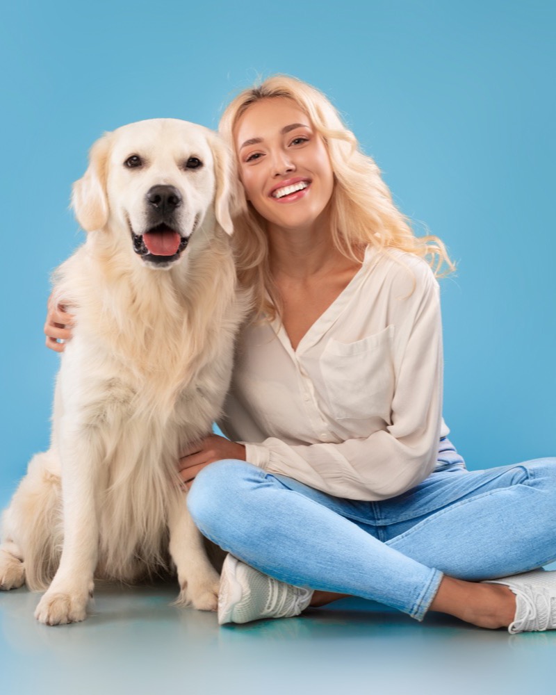 Tutora sorridente sentada no chão abraçando seu golden retriever